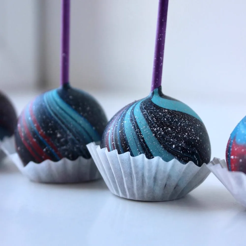 Close-up of dark cake pops with blue swirls in paper cups - Popcakes Ottawa