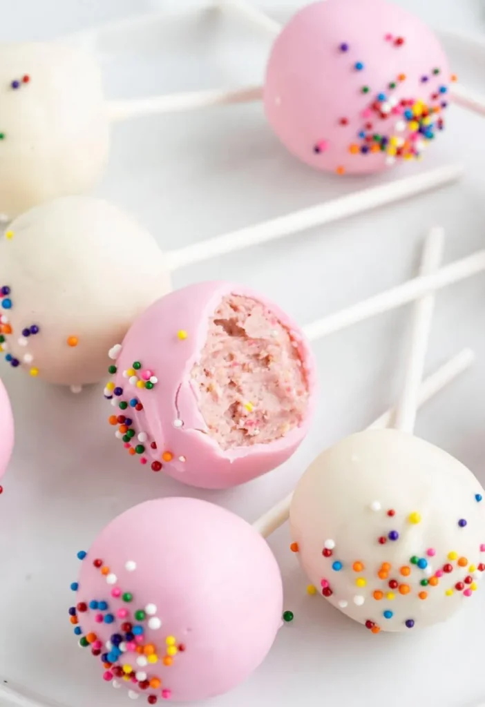 Pink and white cake pops with rainbow sprinkles, one bitten - Popcakes Ottawa